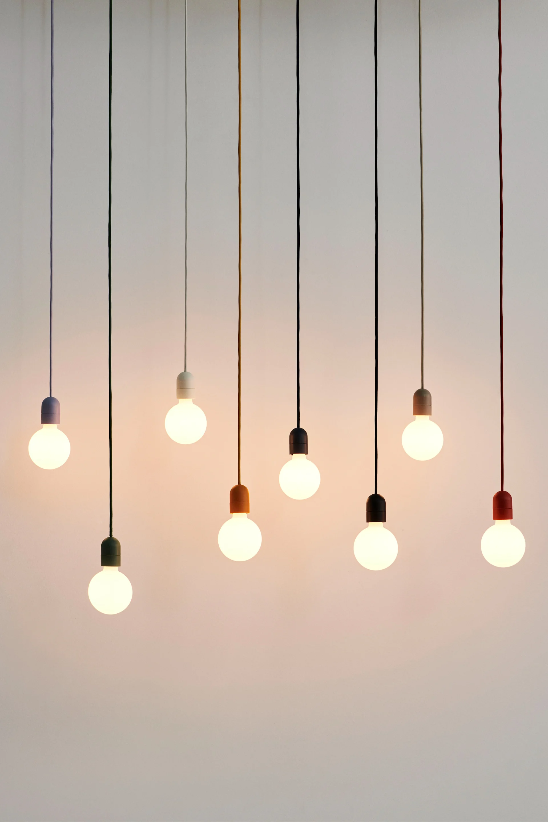 The Muuto E27 lamps hanging in a collection with multi coloured cables. 