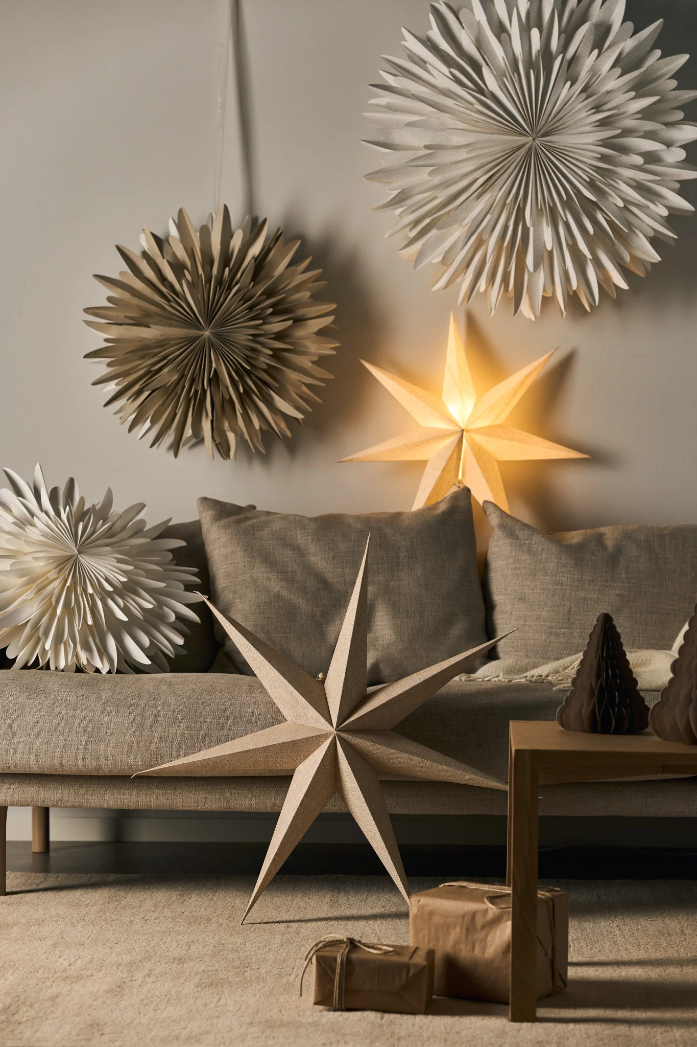 A collection of paper star lanterns hanging above or laid on a sofa in a beige living room. 