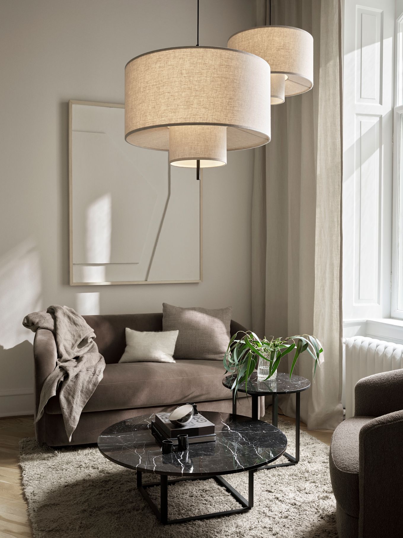 Zwei Pendelleuchten von New Works hängen über einem Couchtisch in einem hellen Wohnzimmer. Mehrere Pendelleuchten zusammen aufzuhängen ist eine einzigartige Idee für die Wohnzimmerbeleuchtung. 