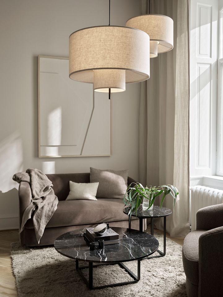 Två pendellampor från New Works hänger över ett soffbord i ett ljust vardagsrum. Att hänga flera pendellampor tillsammans är en unik idé för belysning i vardagsrummet. 