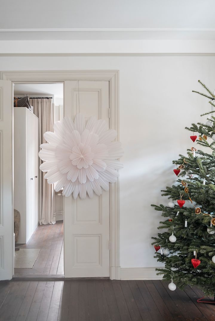 The Snöblomma paper star lantern from Watt & Veke in a huge 100cm hanging in the doorway of a living room next to a Christmas tree. 