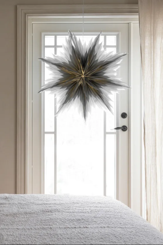 The popular paper star lantern Oslo from Watt och Veke in grey hangings in the window of a cosy bedroom. 
