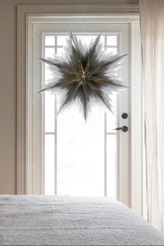 The popular paper star lantern Oslo from Watt och Veke in grey hangings in the window of a cosy bedroom. 