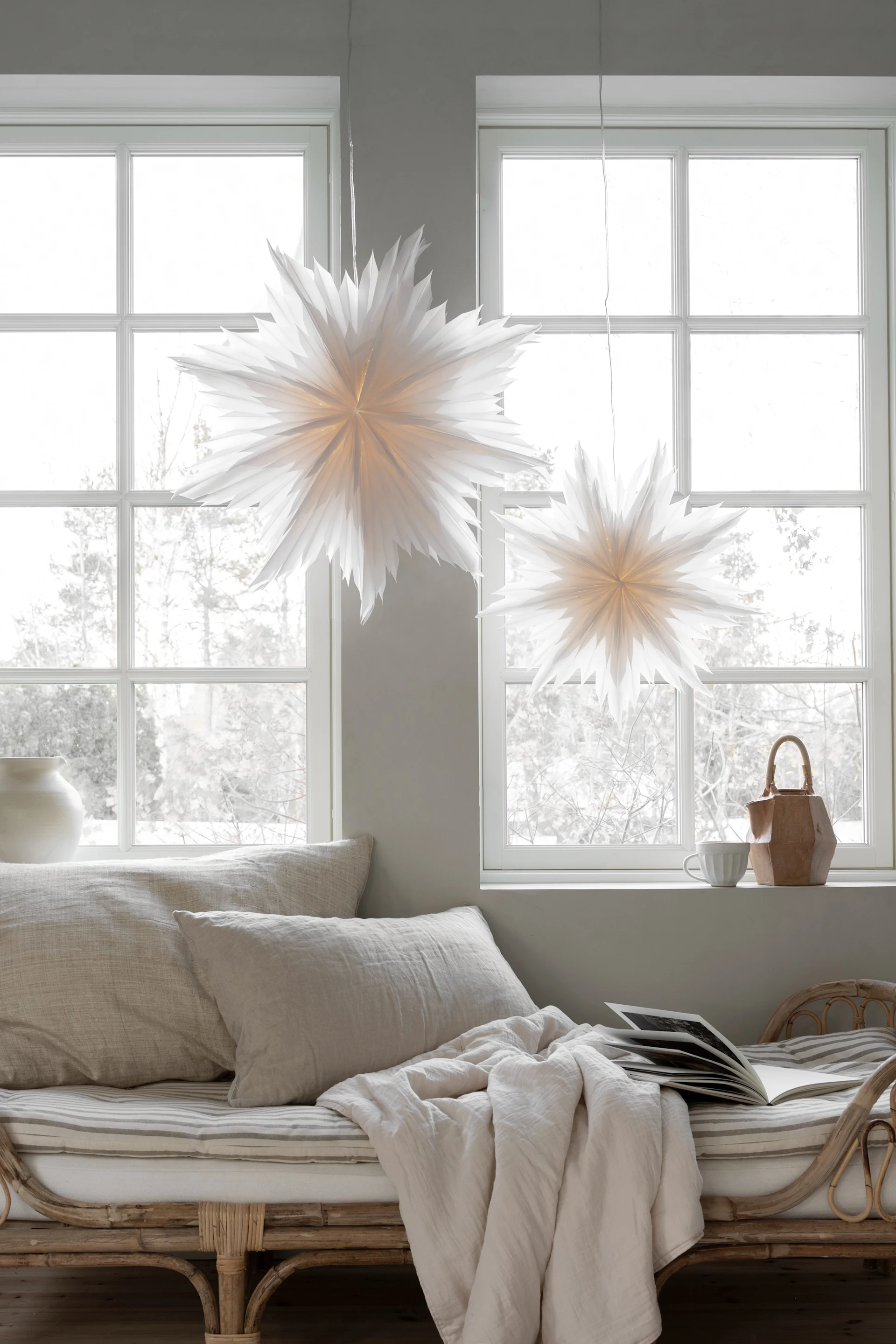A pair of the popular Oslo paper star lanterns from Watt & Veke hang in living room window with a wintery scene outside. 
