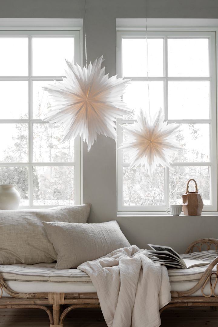 A pair of the popular Oslo paper star lanterns from Watt & Veke hang in living room window with a wintery scene outside. 
