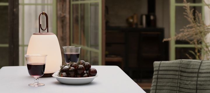Lucca-lampan från &tradition står i en trädgård med glas med rött vin och druvor. 