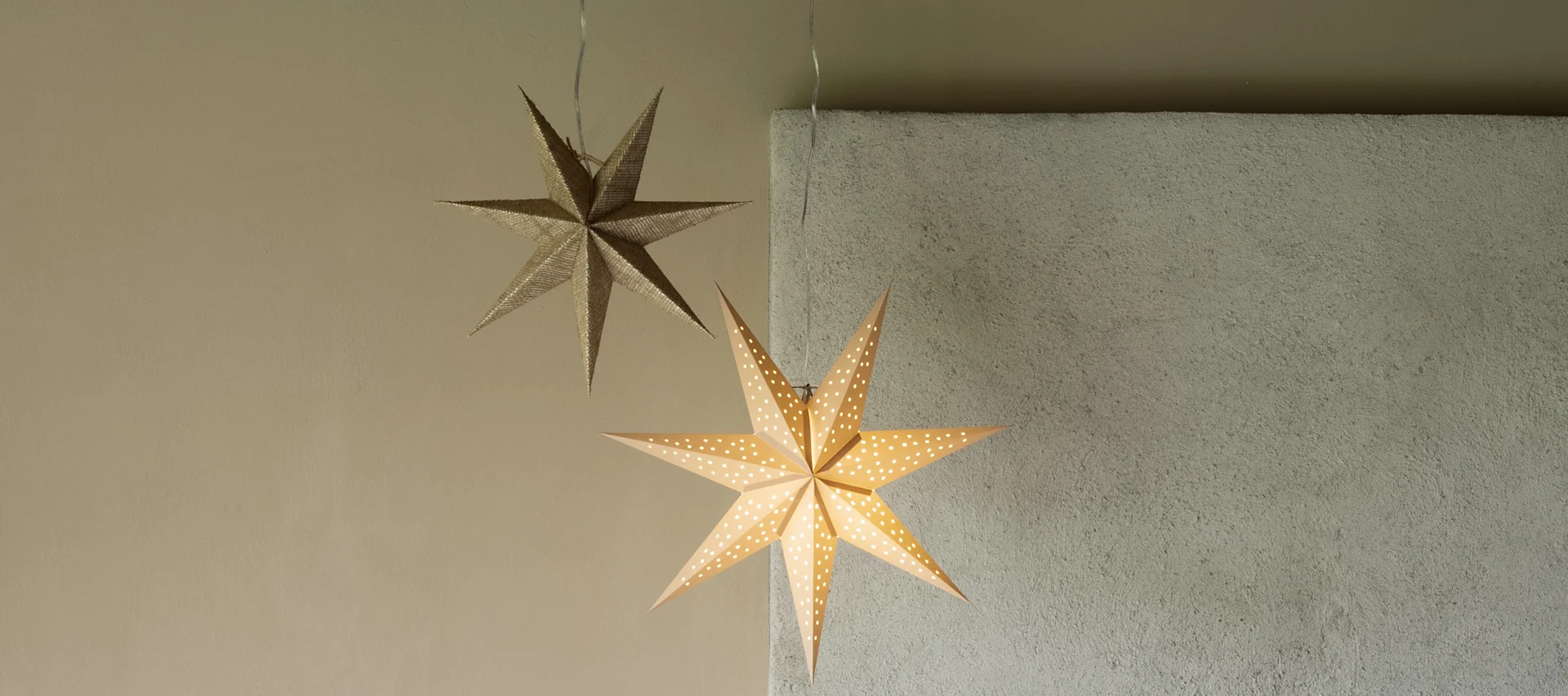 A pair of glowing paper star lanterns from Globen lighting hanging together in a beige living room.